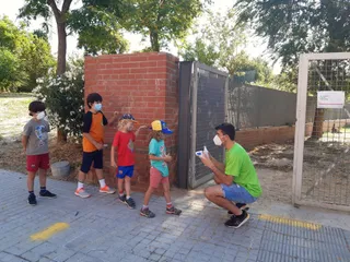 Diversos niños y niñas hacen cola junto a un monitor de tiempo libre
