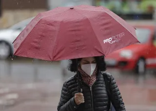 Transeúntes protegidos con mascarilla y un paraguas caminan por las calles de la capital un día marcado por la llegada a la península de una borrasca fría que ha activado la alerta por viento o ll