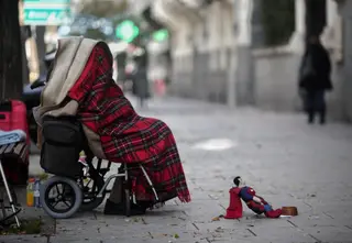 Una persona en silla de ruedas y tapada con una manta pide dinero. FOTO EP