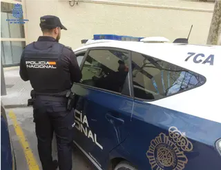 Agente de la Policía Nacional de espaldas, junto a un coche patrulla. - POLICÍA NACIONAL - Archivo