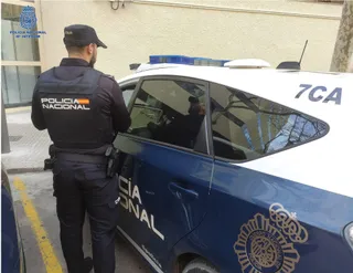 Agente de la Policía Nacional de espaldas, junto a un coche patrulla. - POLICÍA NACIONAL - Archivo