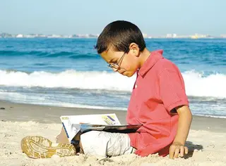 Niño leyendo en la playa | Fotografía Padres y Colegios
