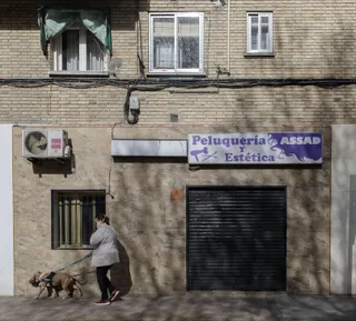 Una mujer pasea a un perro cerca de una peluquería cerrada durante el primer día laborable desde que se decretó el estado de alarma en todo el territorio nacional a consecuencia del coronavirus, en
