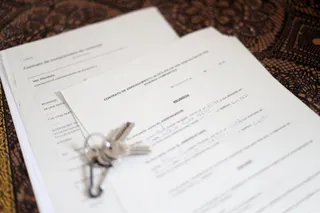 Unas llaves sobre un contrato de compraventa de vivienda y un contrato de arrendamiento (alquiler) de una habitación en una vivienda compartida
