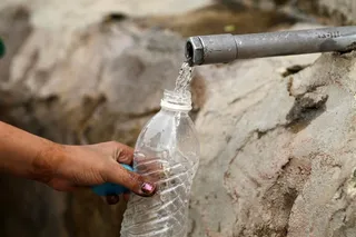 Mujer llenando una botella de agua en un grifo en la calle